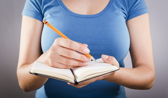 pregnant woman in blue shirt taking notes with pencil and paper notebook