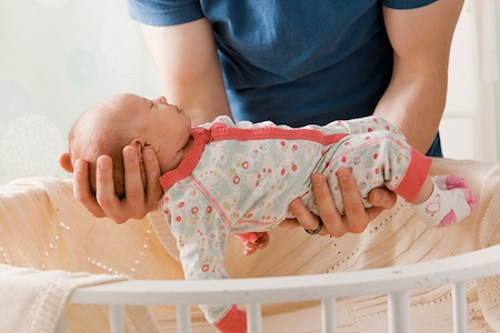 mother holding sleeping newborn baby out of crib supporting head