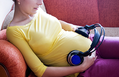 pregnant woman lying on couch with headphones on her stomach