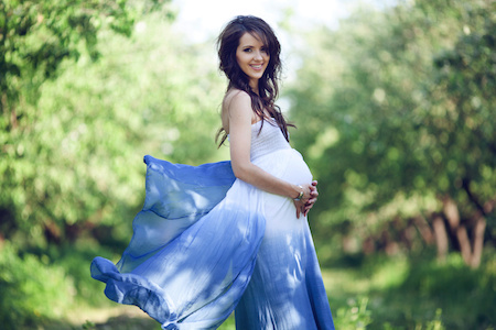 smiling pregnant woman standing outside in a flowing dress