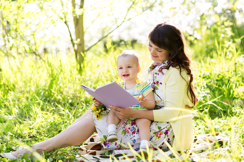woman sitting outside reading a book to her baby