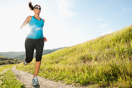 pregnant woman jogging on a trial next to a hillside 